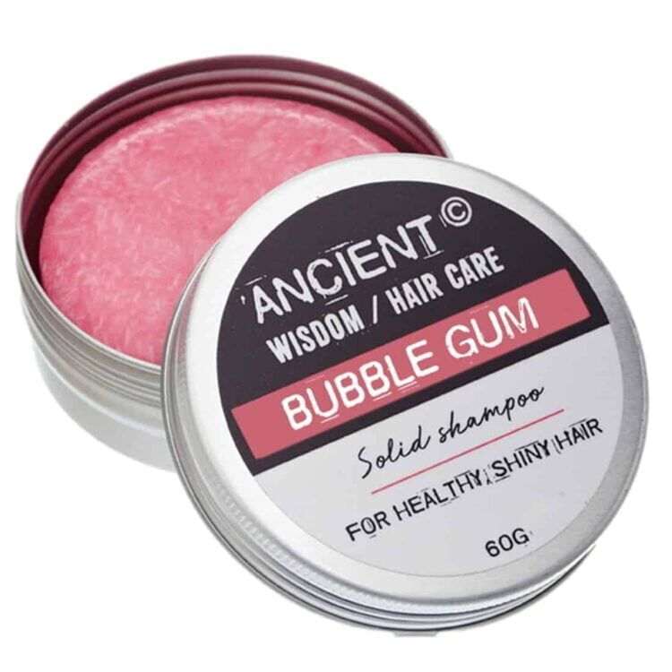 En rund, kompakt shampoo-bar i en lys, pastelrosa nuance. Overfladen har en glat, let skinnende tekstur med små luftbobler, der skaber en interessant visuel effekt. Den er indkapslet i en minimalistisk, hvid emballage med sort tekst, der angiver produktets navn og vægt. Størrelsen er praktisk til håndtering, ideel til rejser.