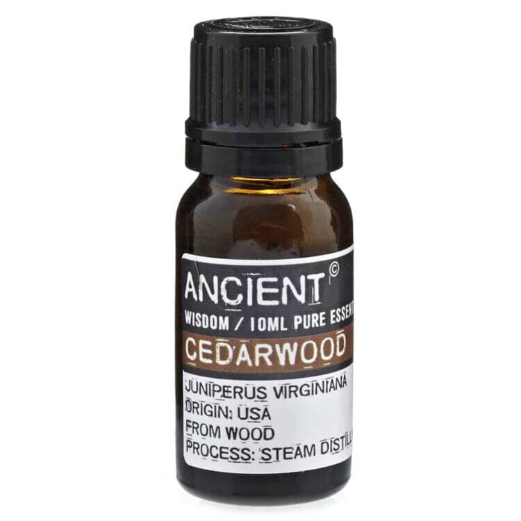 Cedertræ æterisk olie præsenteres i en mørkeblå glasflaske med en sort skruelåg. Flasken har en cylindrisk form og en etiket i nuancerne af hvid og grøn, som angiver produktets navn og indhold. Etiketdesignet inkluderer botaniske illustrationer og tekst i klar skrifttype. Flaskens overflade er glat, hvilket giver et elegant udseende.