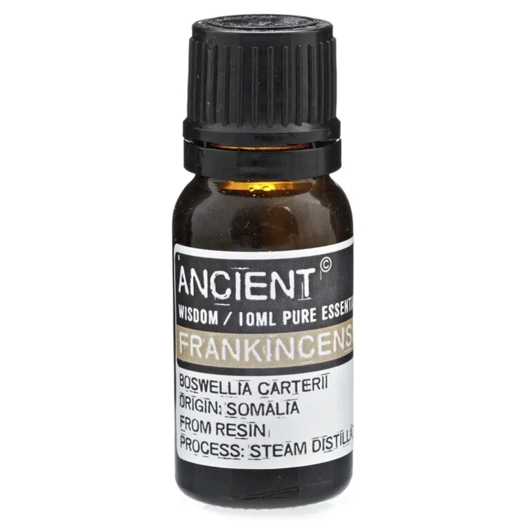 En lille, klar flaske i glas rummer en gyldenbrun æterisk olie. Flasken har en sort, skruelåg med en pipette, der muliggør præcis dosering. Etiket i nuancer af grøn og guld pryder flaskens front, med tydelig skrift, der angiver indholdet. Flasken står på en lys overflade, der fremhæver dens elegante design.