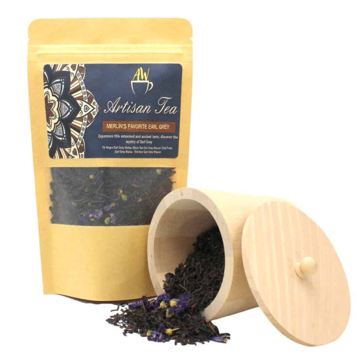 En teæske i en dyb, mørkeblå farve med gyldne detaljer og tekst. Skiltet på forsiden angiver "Merlin's Favorite Earl Grey" med elegante skrifttyper. Æsken har en glat, mat overflade og er rektangulær med afrundede kanter. Indholdet er synligt gennem et gennemsigtigt vindue, der viser teposerne, som har en klassisk, elegant indpakning med mønstre i grå og hvid.