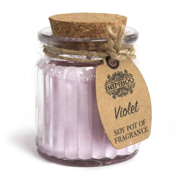 Et lys med en cylindrisk form er placeret i en keramisk krukke, der har en mat, hvid overflade. Voksen er violet og har en glat, blank tekstur. Krukkens kant er let afrundet, og der er en smal, sort bund, der giver kontrast. Ingen synlige etiketter eller teksturer er til stede, hvilket skaber et minimalistisk udtryk.