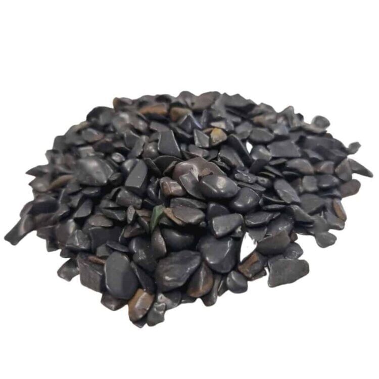 Sort turmalin ligger i en løs samling af små, ujævne chips. De glinsende overflader fanger lyset og fremhæver de dybe, mørke nuancer af sort, fra kulsort til næsten grå. Chipsene varierer i størrelse og form, hvilket giver en organisk tekstur. Nogle stykker har lette, naturlige uregelmæssigheder, der tilføjer karakter til den samlede fremtoning.