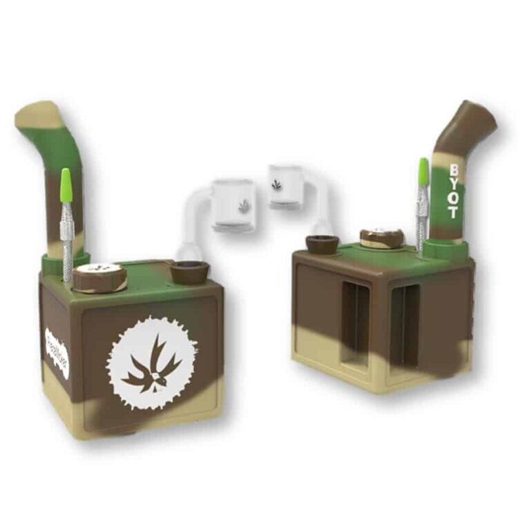 Kube i camouflagefarver præsenterer en firkantet form med bløde hjørner. Overfladen har et struktureret mønster med nuancer af grøn, brun og sort, der skaber en militærinspireret effekt. Det robuste materiale virker slidstærkt, mens små detaljer som syninger og en praktisk håndtag tilføjer en funktionel dimension. Kuben har en minimalistisk og moderne æstetik.