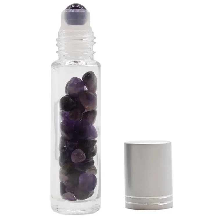 En lilla rollerflaske er præsenteret med en glat, transparent overflade, der skinner let. Flasken har en cylindrisk form med en let udvidelse mod toppen og en afrundet bund. Låget er sølvfarvet med en lille åbning til rullen, som er diskret placeret. Mønsteret på flaskens overflade er simpelt og elegant, uden yderligere dekorationer.