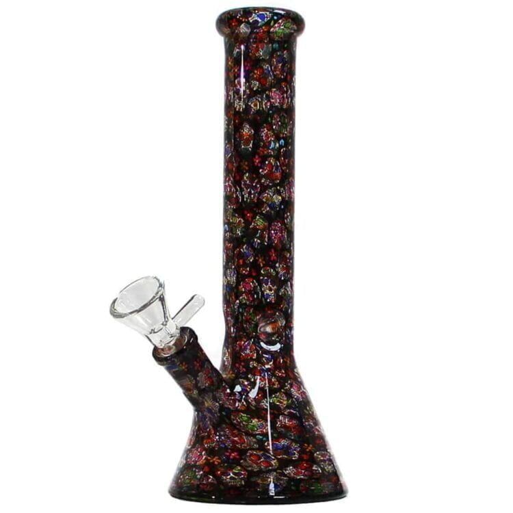 En 26 cm høj bong præsenterer sig med en slank, cylindrisk form. Den er prydet med farverige mexicanske kranier i nuancer af blå, grøn, rød og gul. Materialet er gennemsigtigt glas, hvilket giver en glat overflade. Bongen har en rund base, en lige hals og en skål med en perforeret bund, der muliggør filtrering af røg.