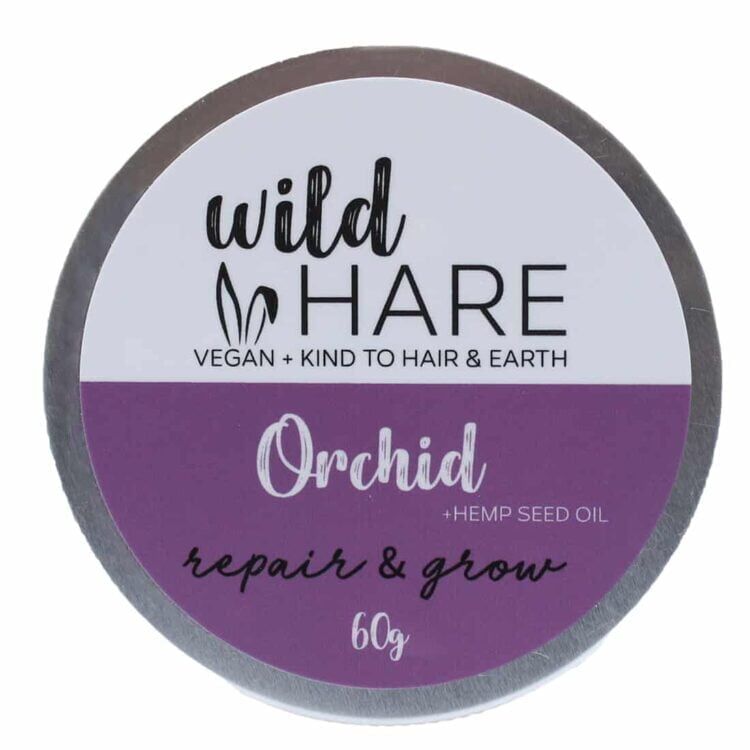 En solid shampoo i form af en cirkulær skive, farvet i en lys lavendelnuance. Overfladen har en glat tekstur med lette, svage skygger, der giver dybde. Indgraverede symboler og tekst pryder overfladen, mens kanterne er let buede. Produktet præsenteres på en neutral, hvid baggrund, hvilket fremhæver farven og detaljerne.