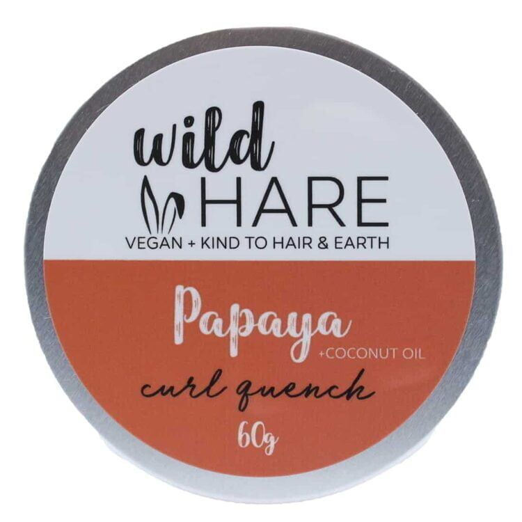 En solid shampoo bar præsenteres i en rund form med en glat, lysebrun overflade, der har en let skinnende finish. Der er små, synlige partikler, der indikerer naturlige ingredienser. På overfladen ses et præg af et logo, der tilføjer et dekorativt element. Størrelsen er kompakt, og den vejer 60 gram.