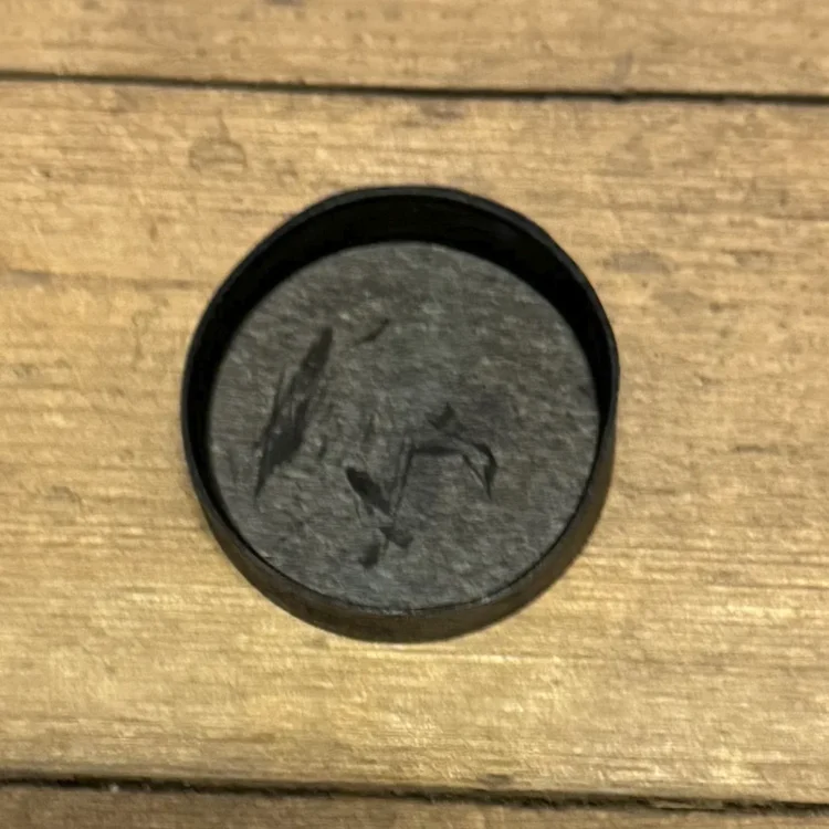 En sort gummihætte præsenteres med en glat, mat overflade. Hætten har en cirkulær form med en let buet top, der skaber et enkelt og funktionelt udtryk. Den indvendige kant er let bølget, hvilket giver en tætsiddende pasform. Ingen synlige sømme eller dekorationer findes, hvilket understreger det minimalistiske design.