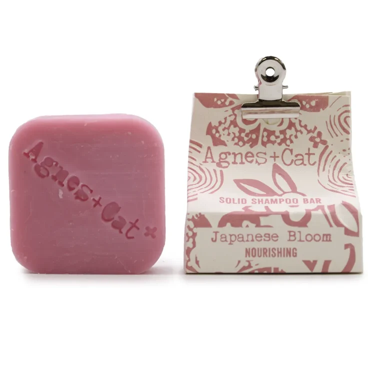 En solid shampoo bar med en rund form præsenterer sig i en blød, pastelgrøn nuance. Overfladen har en let struktureret tekstur, der giver et naturligt udseende. Øverst ses et delikat mønster, der minder om blomster, i en lysere grøn farvetone. Baren er kompakt og har en glat kant, der fremhæver dens enkle design.