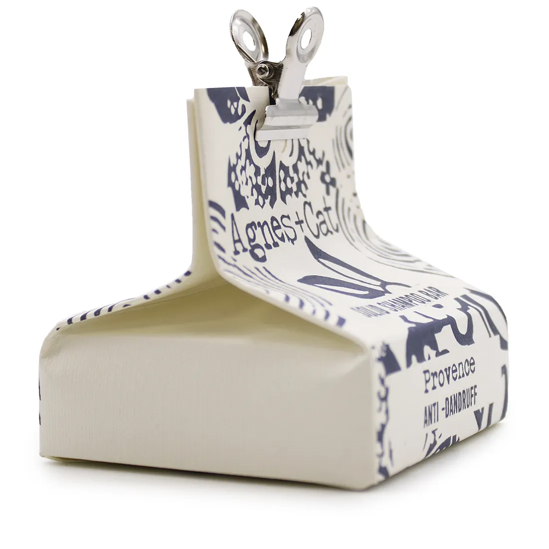 En solid shampoo bar præsenteres i en firkantet form med afrundede hjørner. Overfladen har en glat, ensartet tekstur i en lys, beige farve. Der er en subtil, naturlig duft, som antydes af en let, organisk farvevariation. Ingen synlige emballager eller etiketter er til stede, hvilket fremhæver produktets minimalistiske design.