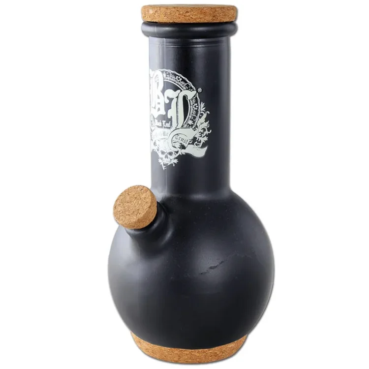 En sort bong med en slank, cylindrisk form præger midten af beskrivelsen. Den har en glat, glansfuld overflade, der reflekterer lys subtilt. Øverst ses en stor, klar glaskugle, der fungerer som en skål. Der er en bøjelig slange i transparent materiale, der tilsluttes bongens side. Bunken har en rund base, der giver stabilitet.