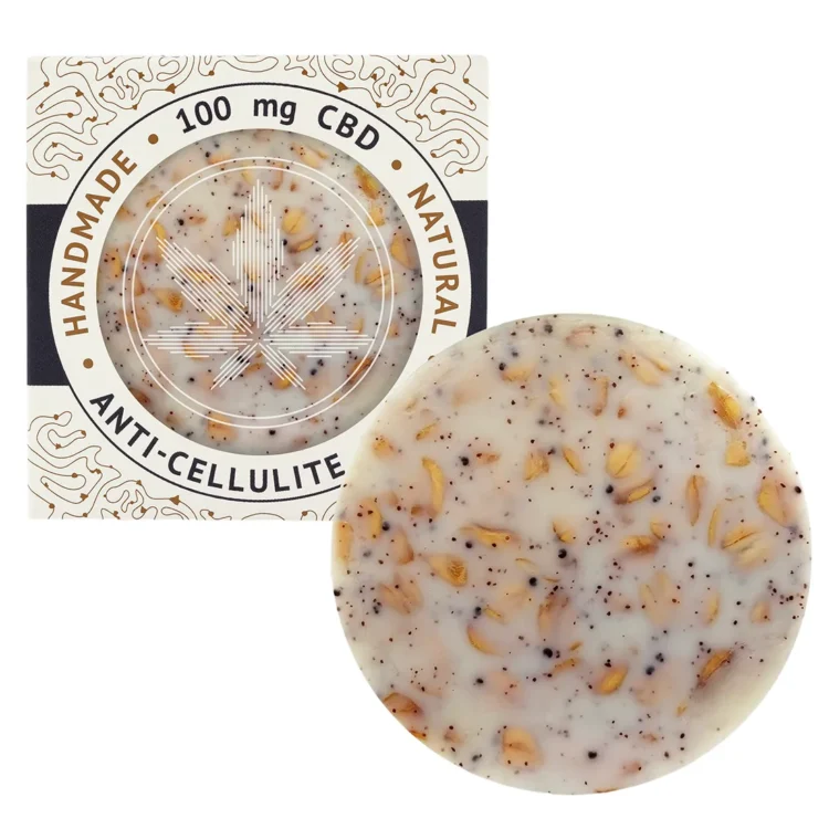 Sæben har en oval form og en glat overflade med en lys, gullig-brun farve. Den er dekoreret med små, mørkere partikler, der tilføjer tekstur. Overfladen har en let skinnende finish, hvilket indikerer fugtighed. Foran ses en indgraveret tekst, der angiver produktets navn og egenskaber, mens kanterne er let afrundede.