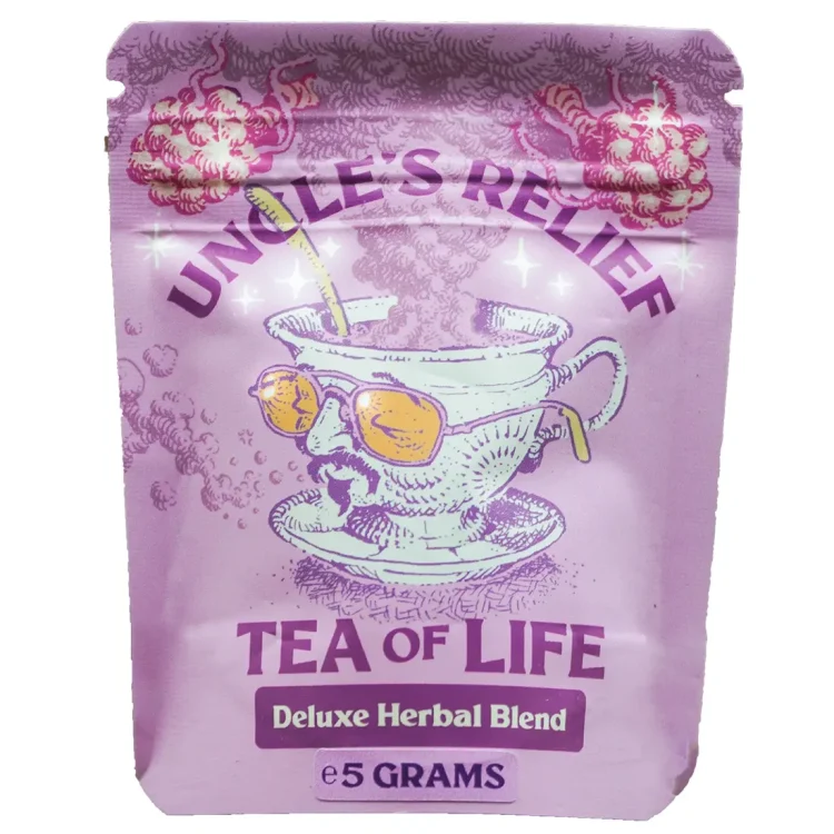 En tepose med en dyb lilla farve hænger fra en snor, som er fastgjort til en papirlabel. Labelen bærer teksten "Tea of Life" i hvid skrift. Teposen har en blød, let gennemsigtig tekstur, mens snoren er tynd og hvid. Baggrunden er neutral og kontrasterer med den intense lilla farve, hvilket fremhæver teposens visuelle tiltrækning.