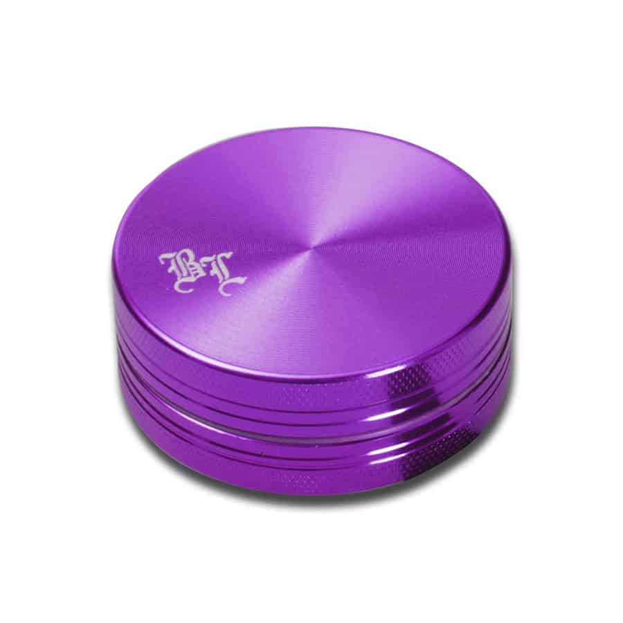 En sort ukrudtsgrinder med en diameter på 50 mm præsenterer en glat, mat overflade. Den har en enkel, cylindrisk form og er dekoreret med et bladmotiv i lilla. Grinderen har tre sektioner, hvor den øverste del indeholder skarpe tænder til formaling. Der er små lufthuller i bunden for effektiv opbevaring af det malede materiale.