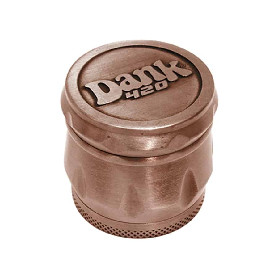 En bronzefarvet kværn pryder overfladen med en let struktureret, præget finish. Den runde form har en skruelås i toppen, der muliggør åbning. Kværnen har en glat, poleret kant og synlige, mekaniske dele inde i enheden. Det samlede design fremstår robust med en mat overflade, der reflekterer lys svagt.