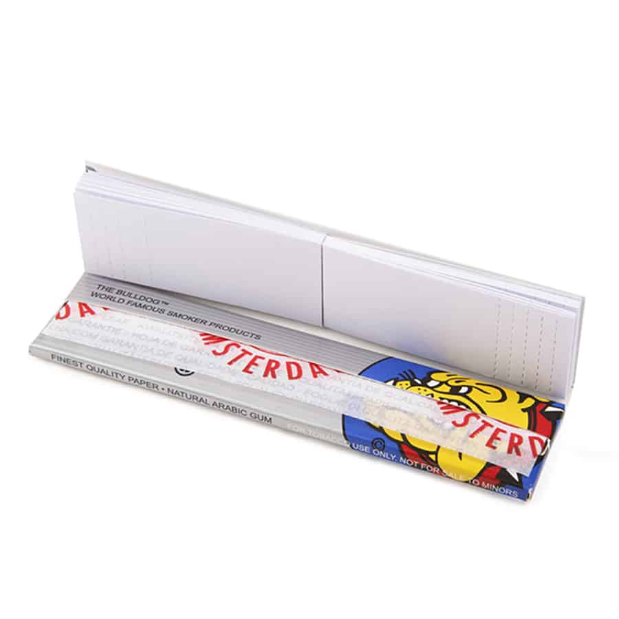 En sølvfarvet pakke med slank, langstrakt form præsenterer sig. Forsiden har et enkelt design med et tydeligt logo og navnet "The Bulldog Amsterdam" i sort skrifttype. Kanten er præget af en mat tekstur, mens baggrunden har en let skinnende overflade. En guldfarvet streg løber langs kanten, hvilket tilføjer kontrast og elegance.