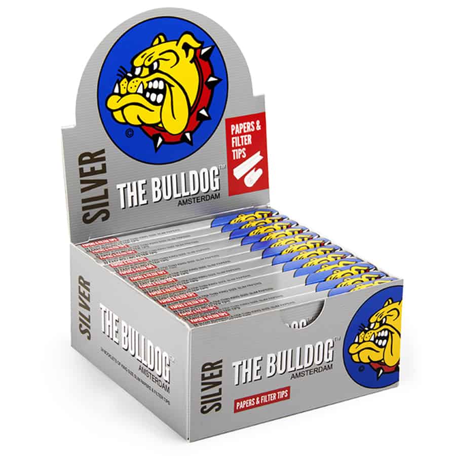 En sølvfarvet boks med en glat overflade, prydet med en sort og hvid etikette. Etiketens design inkluderer en stiliseret bulldog og teksten "King Size Slim M" i sorte bogstaver. Boksen har en rektangulær form med afrundede kanter og en let glans. Den lukkes med en flap, der er integreret i boksens struktur.
