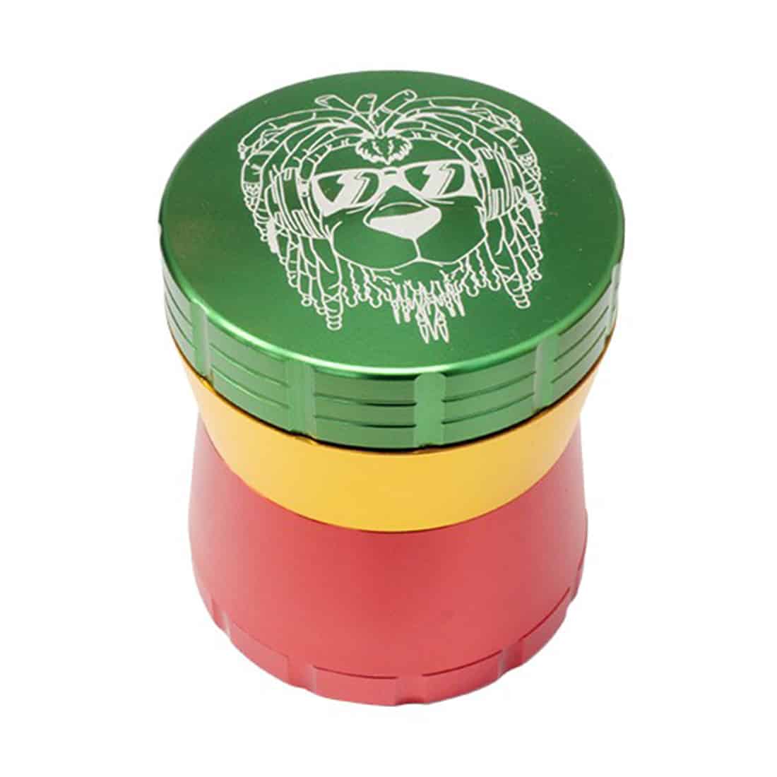 En lille kvadratisk kaffekværn med en diameter på 56 mm præsenteres i et farverigt rasta-design. Overfladen er glat med en kombination af grønne, gule og røde nuancer, der skaber et mønster. Kværnens top har en rund form med en metalknap i midten, og den nederste del har en skridsikker tekstur for bedre greb.