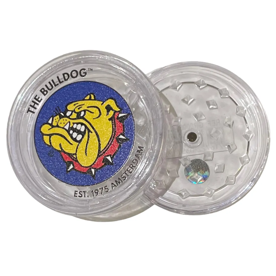 En klar kvadratisk kværn med en diameter på 60 mm. Den har en gennemsigtig plastoverflade, der afslører de indvendige metalstænger og tænder. Kværnen er opdelt i to sektioner med en skruemekanisme til at åbne og lukke. Der er et let skridsikkert mønster på kanten for bedre greb. Den har en glat, blank finish, der fremhæver dens materialer.