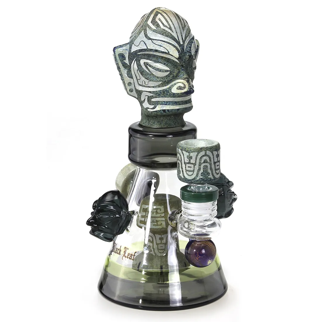 En diffusorbong i sort glas med en oval form pryder overfladen. Den har en glat, blank tekstur og er dekoreret med blade i et stiliseret mønster, der skaber en kontrast til det matte glas. Bongen har en krum hals og en bred bund, hvilket giver stabilitet. Det elegante design fremhæver formerne og detaljer i strukturen.