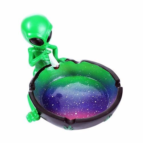 Et askebæger i høj, oval form fremstillet af klart glas. Overfladen er glat med en let bølget kant, der giver et elegant udtryk. Indvendigt er der en dybning til aske, mens ydersiden har en let krystalagtig struktur, der reflekterer lyset. Farven er transparent med subtile nuancer af grønt, der tilføjer dybde.