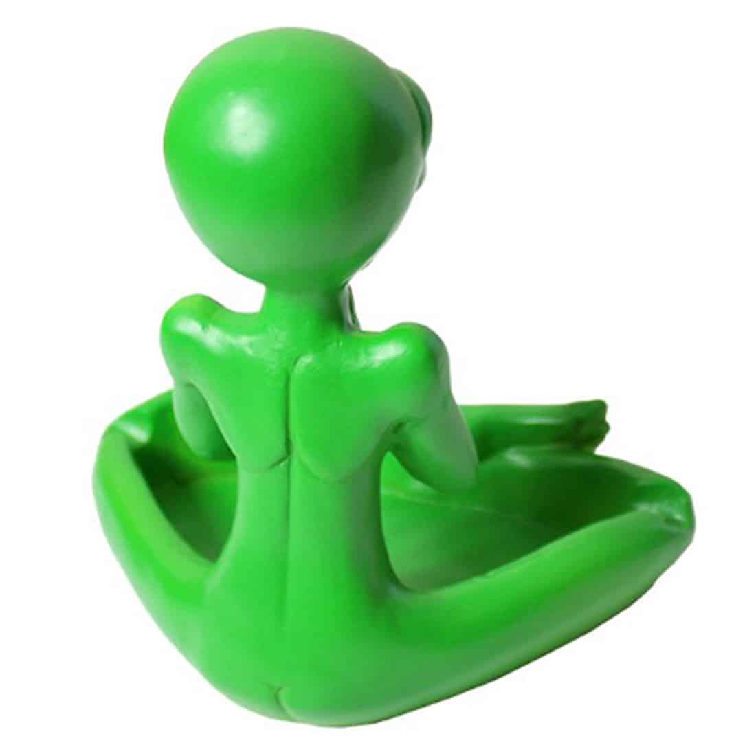 Et askebæger i form af en grøn alien figur pryder overfladen. Alienens hoved er stort og rundt med store, sorte øjne og en bred mund. Krop og arme er korte og klumpede, mens farven er ensartet grøn med en glat overflade. Bunden er flad og stabil, hvilket sikrer, at askebægeret står sikkert.