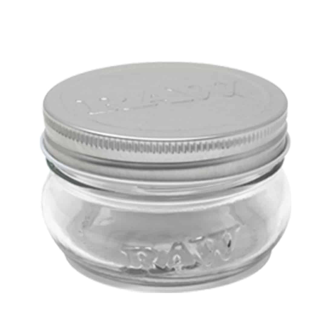 Et klart glas syltetøjsglas med en skruelåg, der har en metaloverflade. Glasset har en cylindrisk form og en let konisk bund, hvilket giver det stabilitet. Låget er sølvfarvet med en glat overflade, mens glasset er transparent og fremhæver indholdet. På glasset ses en label med skrå skrift, der angiver volumen på 177 ml.