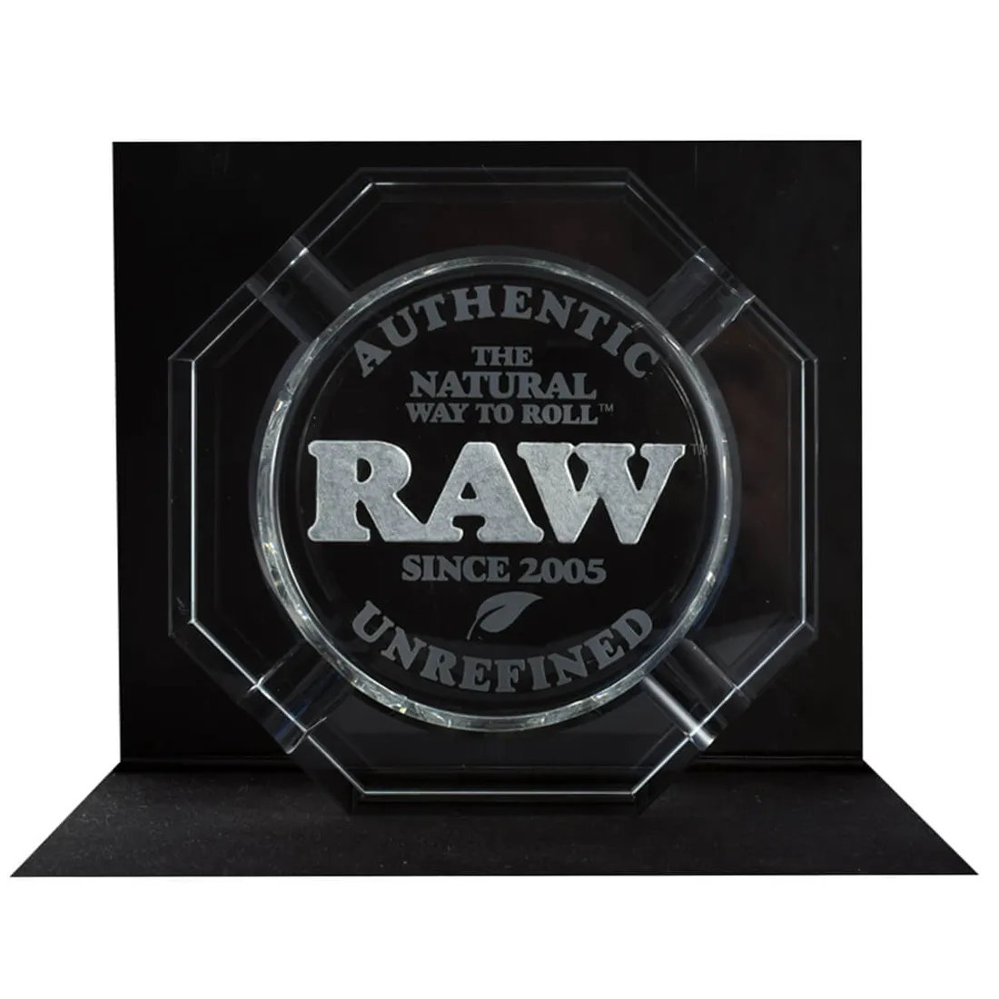 Et askebæger fremstillet af rå krystal præsenterer en uregelmæssig, organisk form med ujævne kanter. Overfladen skinner med en klar, gennemsigtig tekstur, hvor lys reflekteres og brydes, hvilket skaber et glitrende udtryk. Farven er næsten farveløs med subtile nuancer af grå og hvid, der fremhæver de naturlige mineralstrukturer i krystallen.