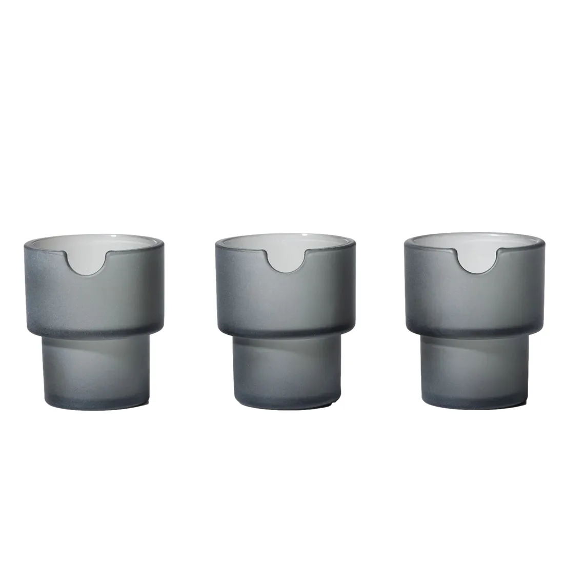 Askeholderen har en cylindrisk form med en glat, mat overflade i en dyb, mørkegrå farve. Den er fremstillet af keramik, hvilket giver en robust og elegant fremtoning. Øverste kant er let afrundet, og bunden er flad for stabilitet. Den har en diskret, indgraveret tekstur, der tilføjer et subtilt visuelt element til designet.