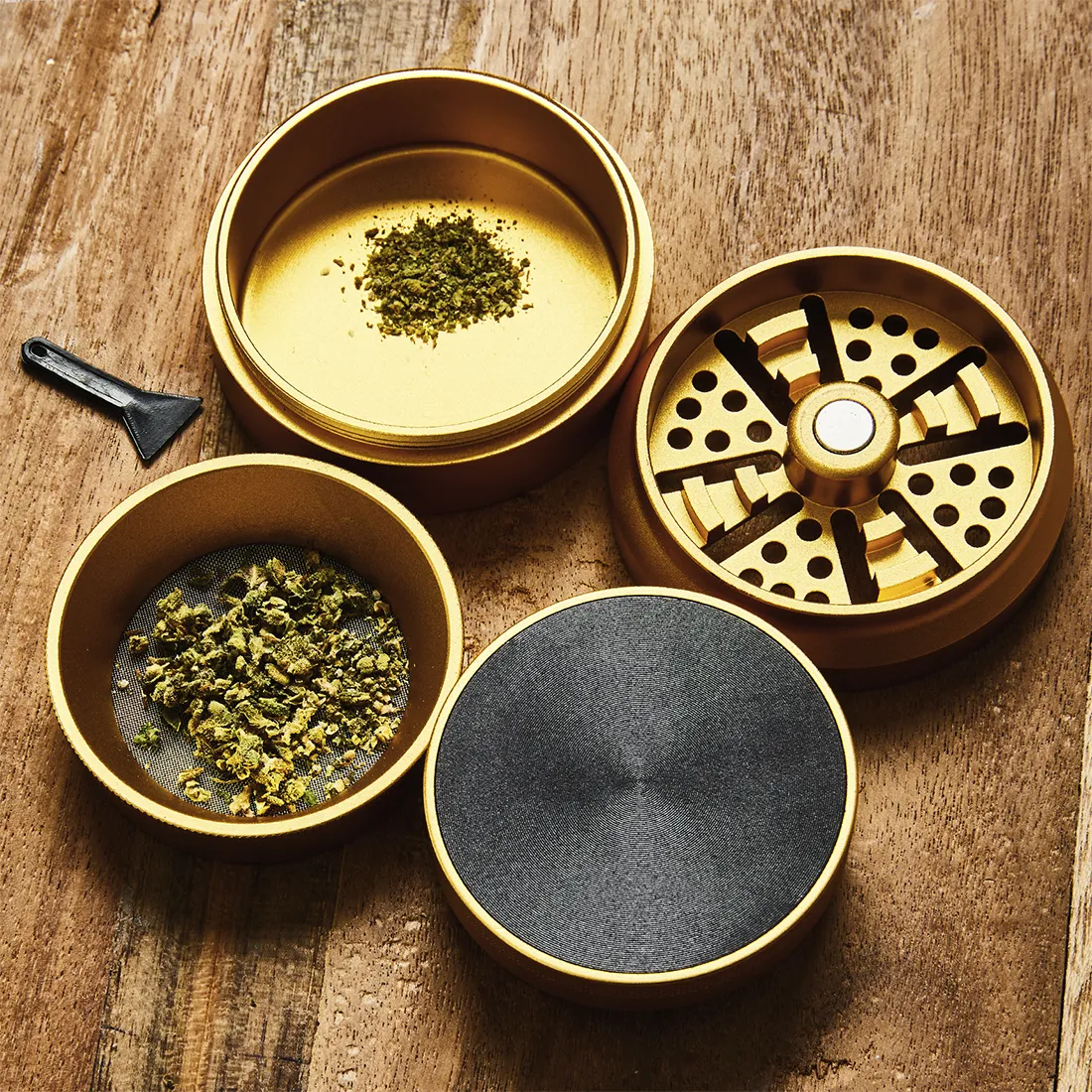 En gylden kværn med en diameter på 55-63 mm præsenterer sig med en glat, metallisk overflade. Den har et fladt låg med en let buet form og en indgravering, der tilføjer detaljer. Kværnen er opdelt i sektioner med små tænder, der skaber en skarp kontrast til den ensartede overflade. Kanten er let afrundet, hvilket giver en behagelig håndtering.