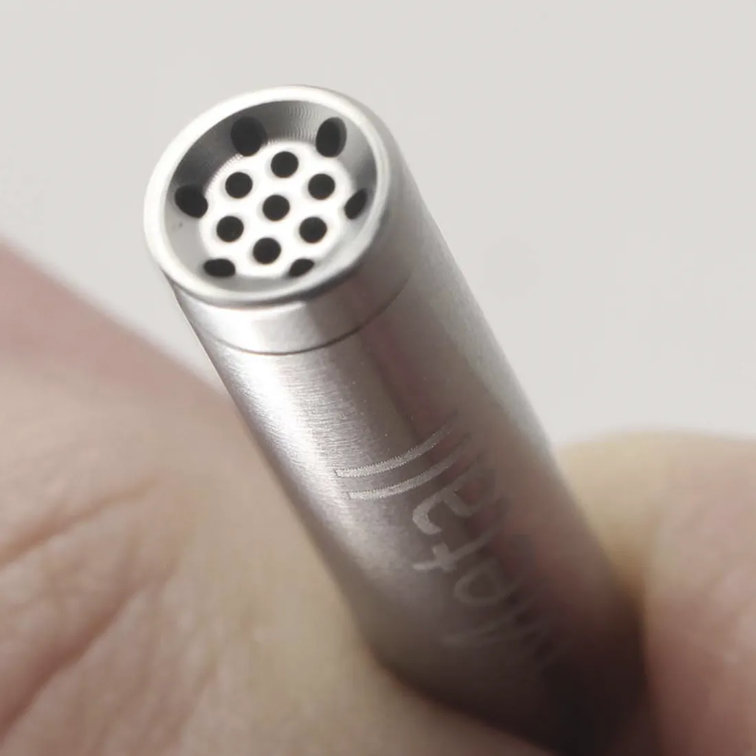 Aktiv kulfiltertips i rustfrit stål præsenterer en slank, cylindrisk form med en glat, poleret overflade, der reflekterer lys. Den har en sølvfarvet nuance, der understreger materialets metaliske karakter. Filtertipsene er forsynet med små perforeringer, der skaber et mønster, og de er placeret i en praktisk opbevaringsæske med en transparent lukning.