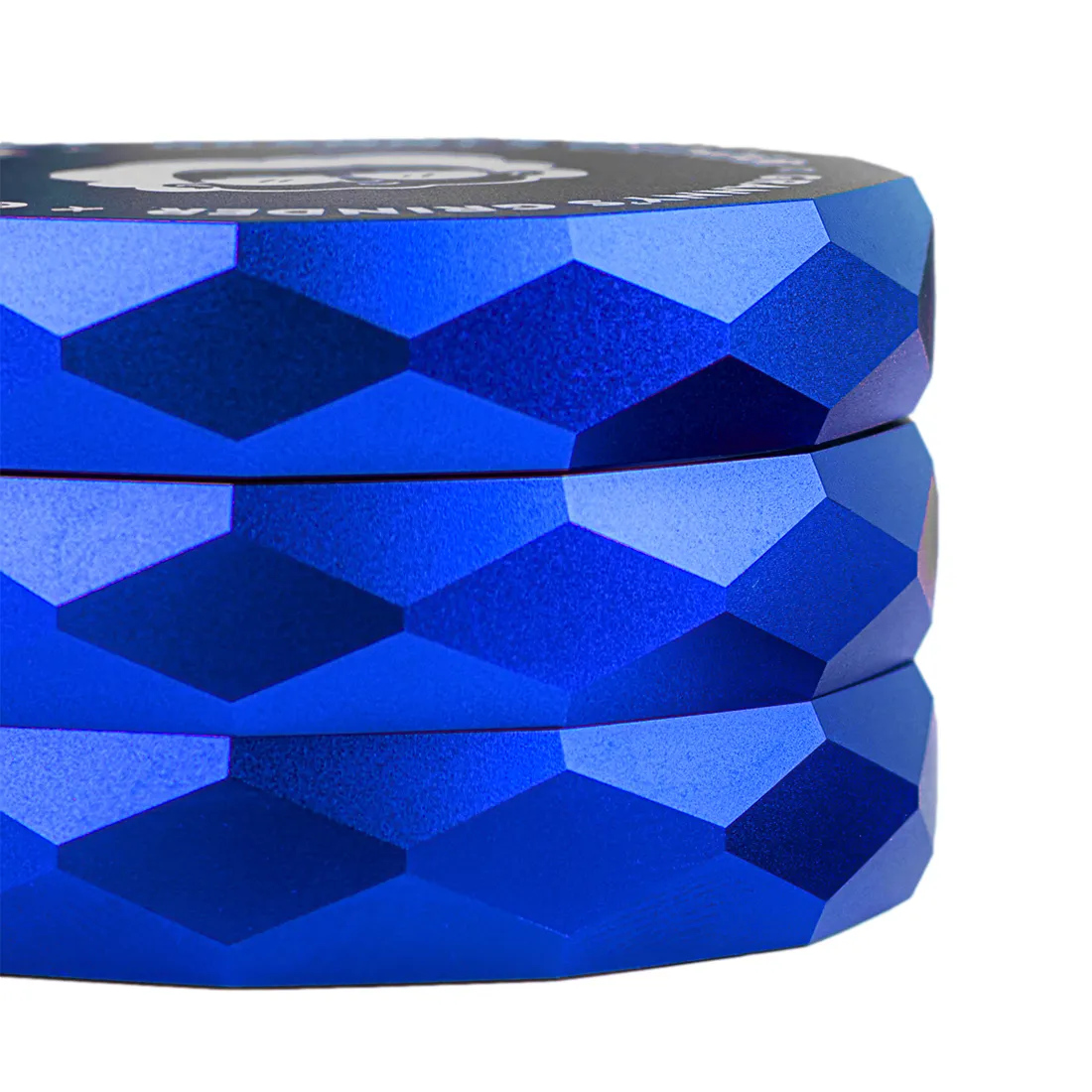 En lille, rund grå grinder med en blå hexagonal mønster på toppen. Den er lavet af metal med en glat overflade og afrundede kanter. Grinderens indre har skarpe tænder til formaling, og der er små huller, der muliggør passage af det formalte materiale. En fin, blå farve pryder toppen, hvilket skaber kontrast til det grå metal.